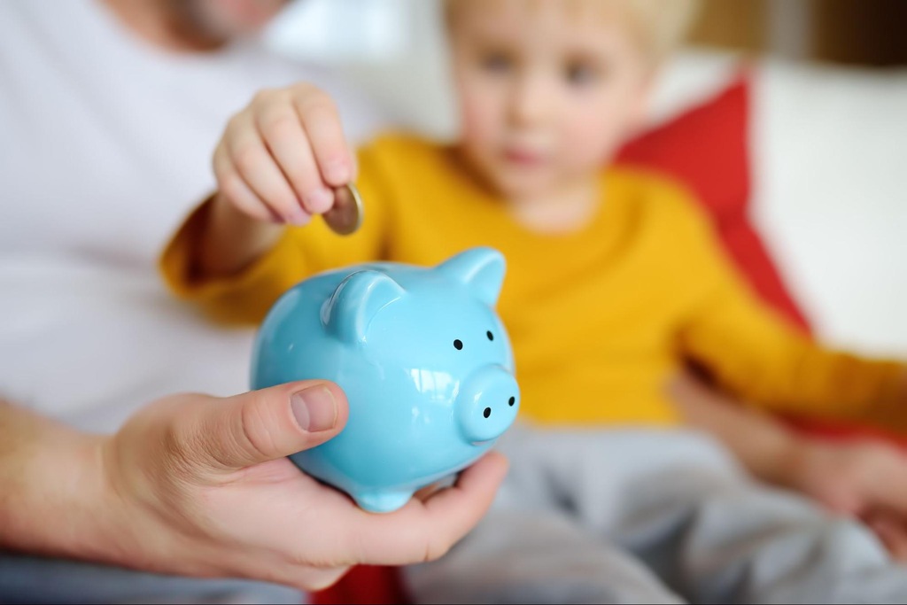 criança colocando moeda em cofre de porquinho após aprender sobre educação financeira infantil