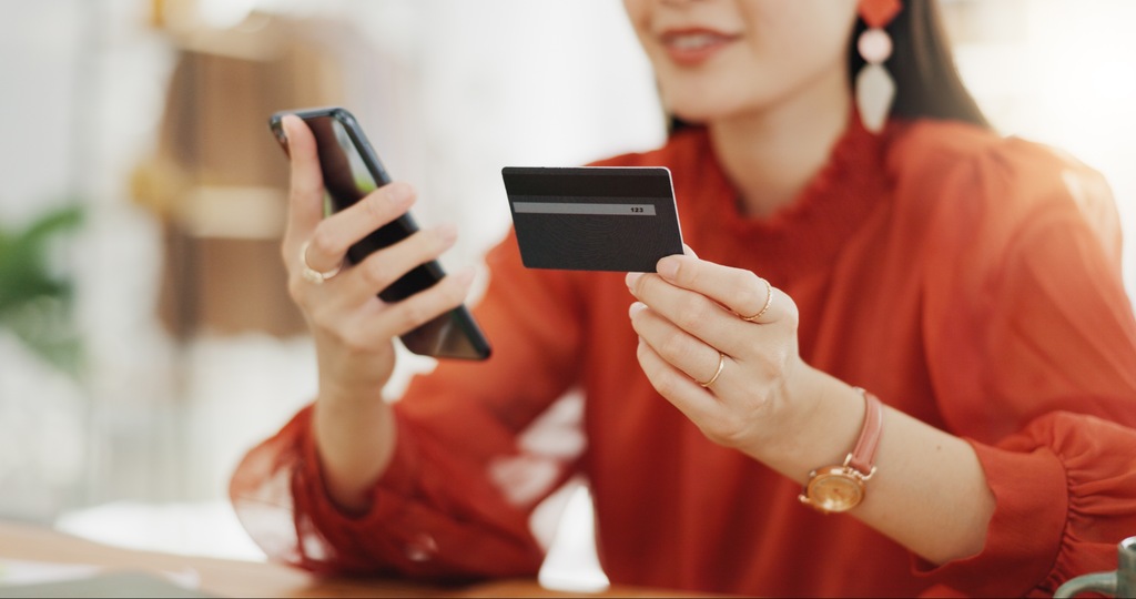 mulher usando celular e cartão do banco digital que rende mais, para realizar investimento