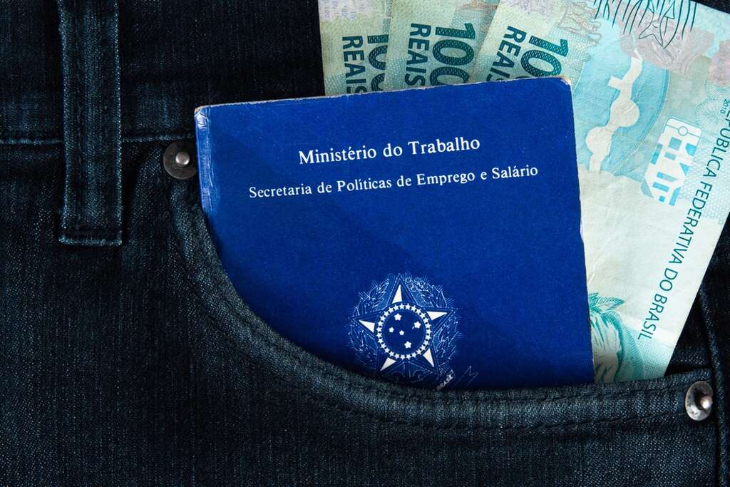 carteira de trabalho ao lado de notas de 100 reais, representando o salário mínimo regional